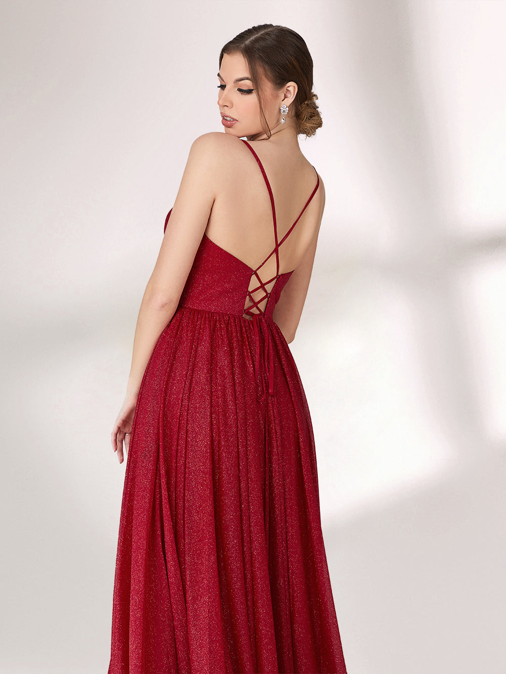 A woman stands against a light background, wearing a deep red evening gown. It has thin spaghetti straps, a deep V - neckline, and a voluminous skirt with a shimmering texture, creating an elegant and glamorous look, perfect for formal events.2