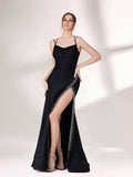 A woman stands against a light - colored background, donning a black evening gown. It has thin spaghetti straps and a gently draped neckline. The gown features a high - side slit adorned with sparkling rhinestones, adding a touch of glamour. The sleek, floor - length skirt is made of a subtly shimmering fabric, creating an elegant and alluring look that's perfect for formal galas or upscale evening events.1