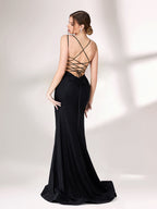 A woman stands against a light - colored background, donning a black evening gown. It has thin spaghetti straps and a gently draped neckline. The gown features a high - side slit adorned with sparkling rhinestones, adding a touch of glamour. The sleek, floor - length skirt is made of a subtly shimmering fabric, creating an elegant and alluring look that's perfect for formal galas or upscale evening events.22