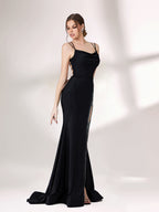 A woman stands against a light - colored background, donning a black evening gown. It has thin spaghetti straps and a gently draped neckline. The gown features a high - side slit adorned with sparkling rhinestones, adding a touch of glamour. The sleek, floor - length skirt is made of a subtly shimmering fabric, creating an elegant and alluring look that's perfect for formal galas or upscale evening events.3