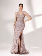 Illuminated softly, a woman captivates in a pink - purple evening gown. With sequin and feather details, a mermaid silhouette, and a high slit, it creates a glamorous and alluring look for formal events.1