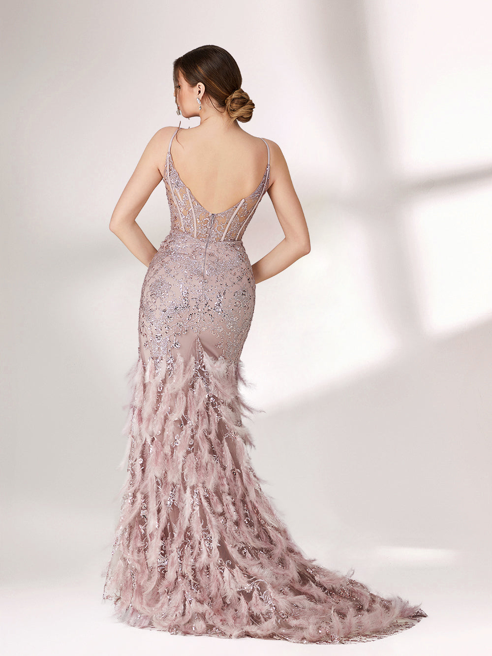 Illuminated softly, a woman captivates in a pink - purple evening gown. With sequin and feather details, a mermaid silhouette, and a high slit, it creates a glamorous and alluring look for formal events.2