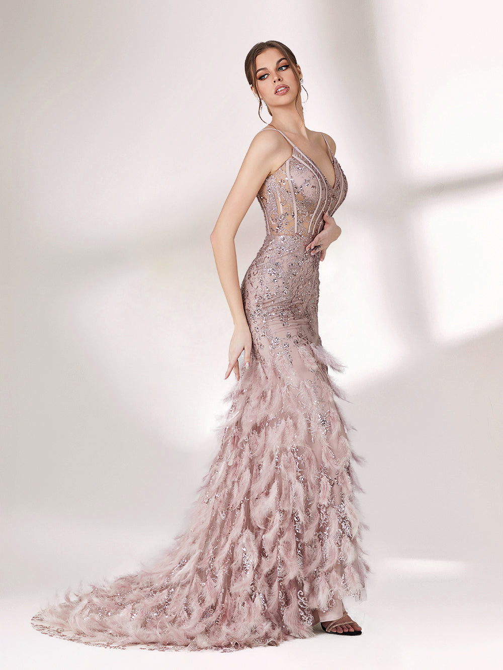 Illuminated softly, a woman captivates in a pink - purple evening gown. With sequin and feather details, a mermaid silhouette, and a high slit, it creates a glamorous and alluring look for formal events.4