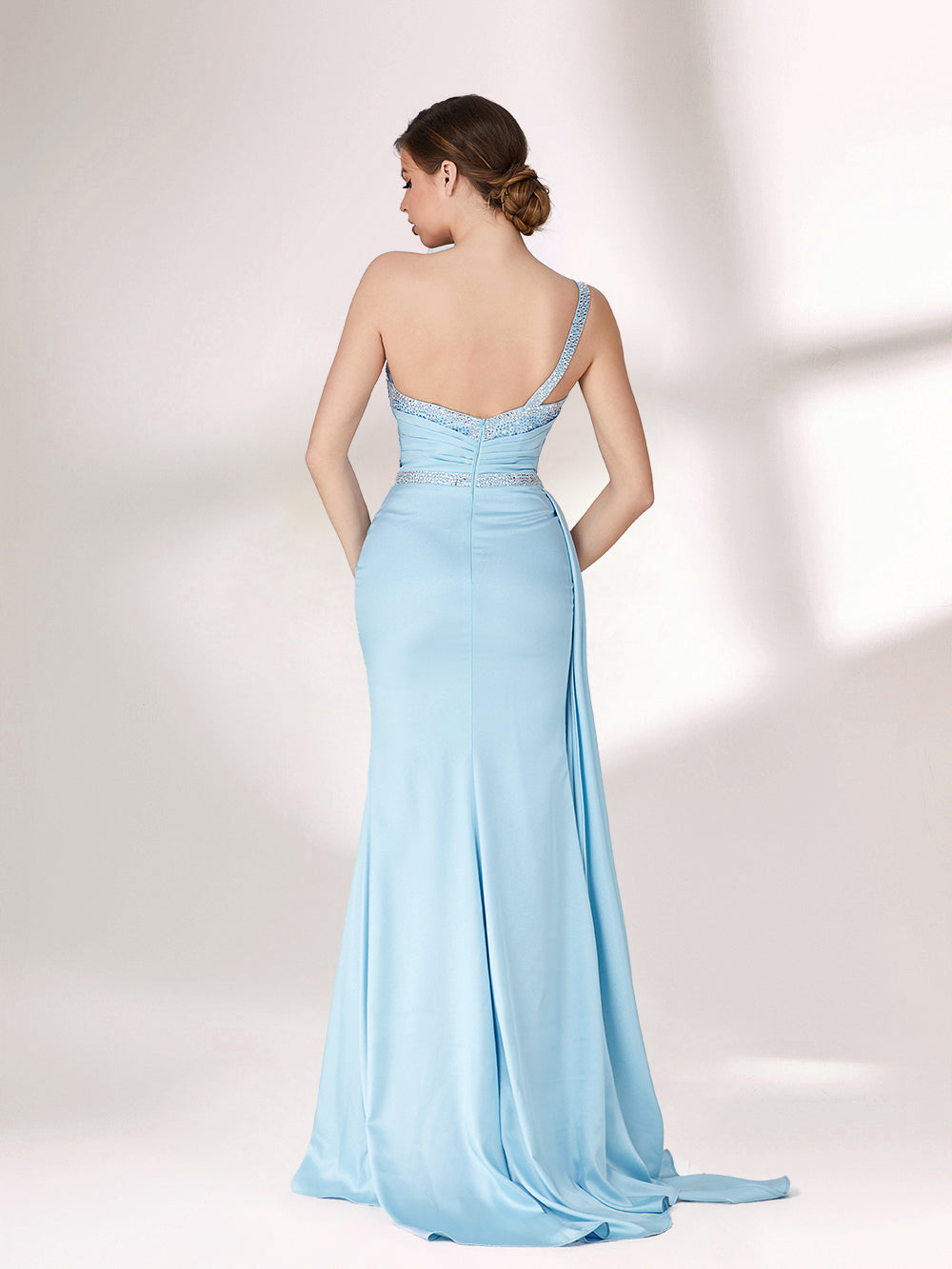 A woman stands against a light background, wearing a light blue evening gown. It has a one - shoulder design, with the bodice adorned with delicate beadwork. A bejeweled waistband cinches the waist, and the skirt, made of smooth satin, flows down to the floor with a small train, creating an elegant and graceful look, perfect for formal events.2