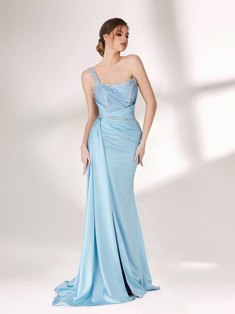 A woman stands against a light background, wearing a light blue evening gown. It has a one - shoulder design, with the bodice adorned with delicate beadwork. A bejeweled waistband cinches the waist, and the skirt, made of smooth satin, flows down to the floor with a small train, creating an elegant and graceful look, perfect for formal events.5