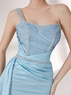 A woman stands against a light background, wearing a light blue evening gown. It has a one - shoulder design, with the bodice adorned with delicate beadwork. A bejeweled waistband cinches the waist, and the skirt, made of smooth satin, flows down to the floor with a small train, creating an elegant and graceful look, perfect for formal events.6