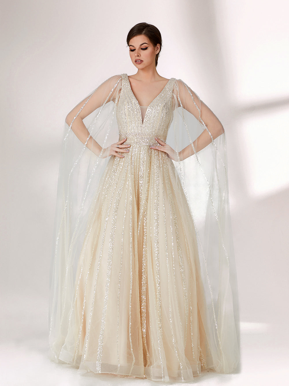 Against a light - hued background, a woman wears an ivory sequin gown with a sheer cape. It features a deep V - neckline, a fitted bodice, and a voluminous skirt. The shimmering sequins and elegant cape design radiate sophistication, perfect for formal events like charity balls, exuding a regal1