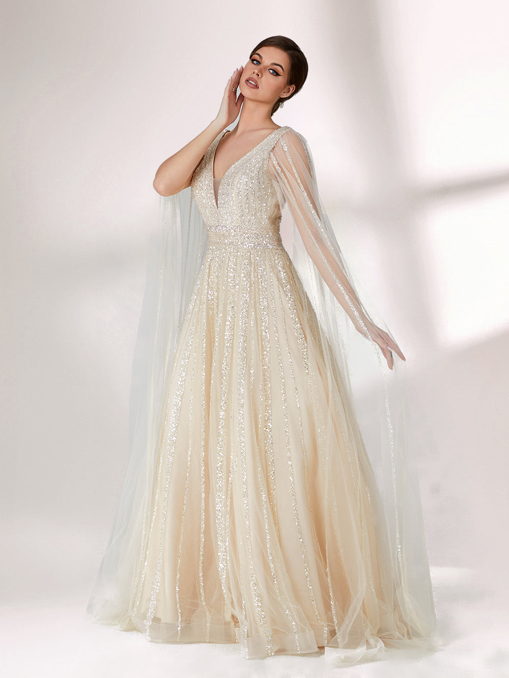 Against a light - hued background, a woman wears an ivory sequin gown with a sheer cape. It features a deep V - neckline, a fitted bodice, and a voluminous skirt. The shimmering sequins and elegant cape design radiate sophistication, perfect for formal events like charity balls, exuding a regal aura.3