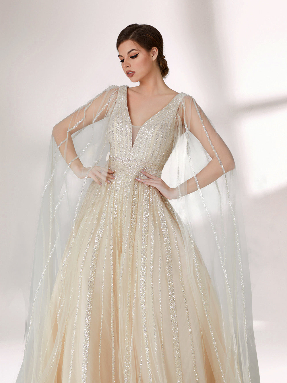 Against a light - hued background, a woman wears an ivory sequin gown with a sheer cape. It features a deep V - neckline, a fitted bodice, and a voluminous skirt. The shimmering sequins and elegant cape design radiate sophistication, perfect for formal events like charity balls, exuding a regal aura.4