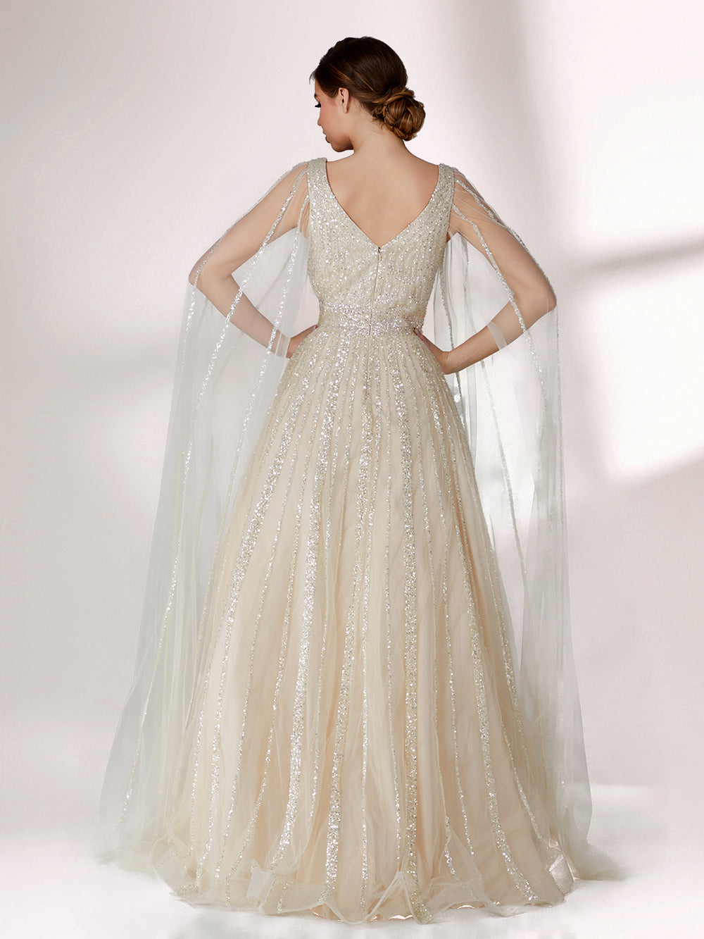 Against a light - hued background, a woman wears an ivory sequin gown with a sheer cape. It features a deep V - neckline, a fitted bodice, and a voluminous skirt. The shimmering sequins and elegant cape design radiate sophistication, perfect for formal events like charity balls, exuding a regal aura.2