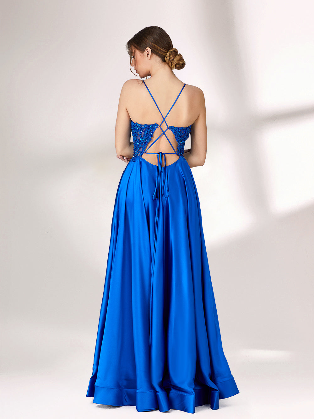 In soft lighting, a woman stuns in a royal blue evening gown. With spaghetti straps, lace detailing, and a high slit, it creates an elegant and bold look for formal events.2