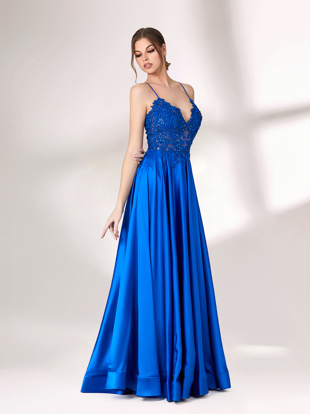 In soft lighting, a woman stuns in a royal blue evening gown. With spaghetti straps, lace detailing, and a high slit, it creates an elegant and bold look for formal events.3