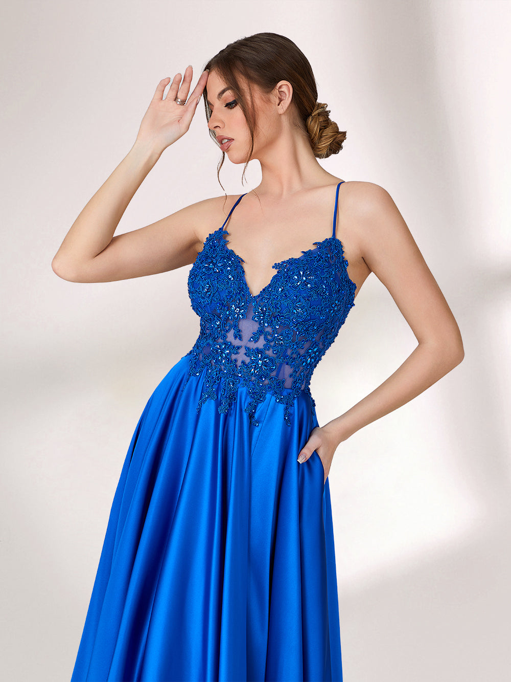 In soft lighting, a woman stuns in a royal blue evening gown. With spaghetti straps, lace detailing, and a high slit, it creates an elegant and bold look for formal events.4