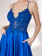In soft lighting, a woman stuns in a royal blue evening gown. With spaghetti straps, lace detailing, and a high slit, it creates an elegant and bold look for formal events.5