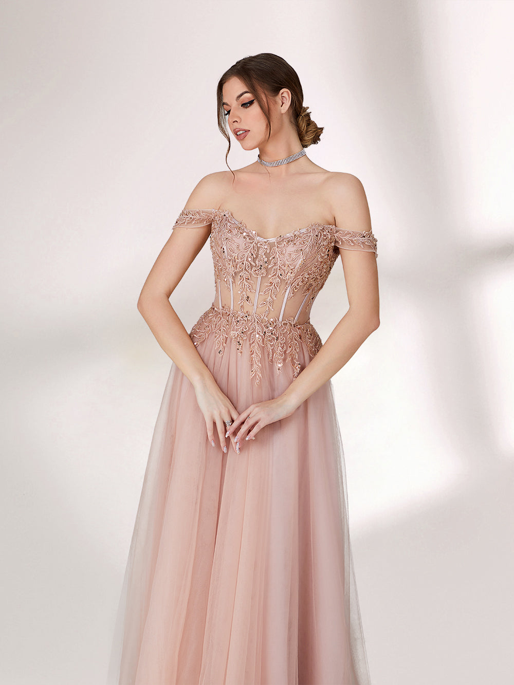 A woman stands against a light background, wearing a blush - pink evening gown. It has an off - the - shoulder design with a sweetheart neckline. The bodice is adorned with intricate lace and bead embroidery, and the skirt is made of flowing tulle, creating an elegant and romantic look, perfect for formal events.