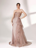 A woman stands against a light background, wearing a blush - toned strapless evening gown. The bodice features intricate floral embroidery, and there's a draped, embroidered tulle overlay on the skirt with a small train. The design is elegant and romantic, suitable for formal events.1