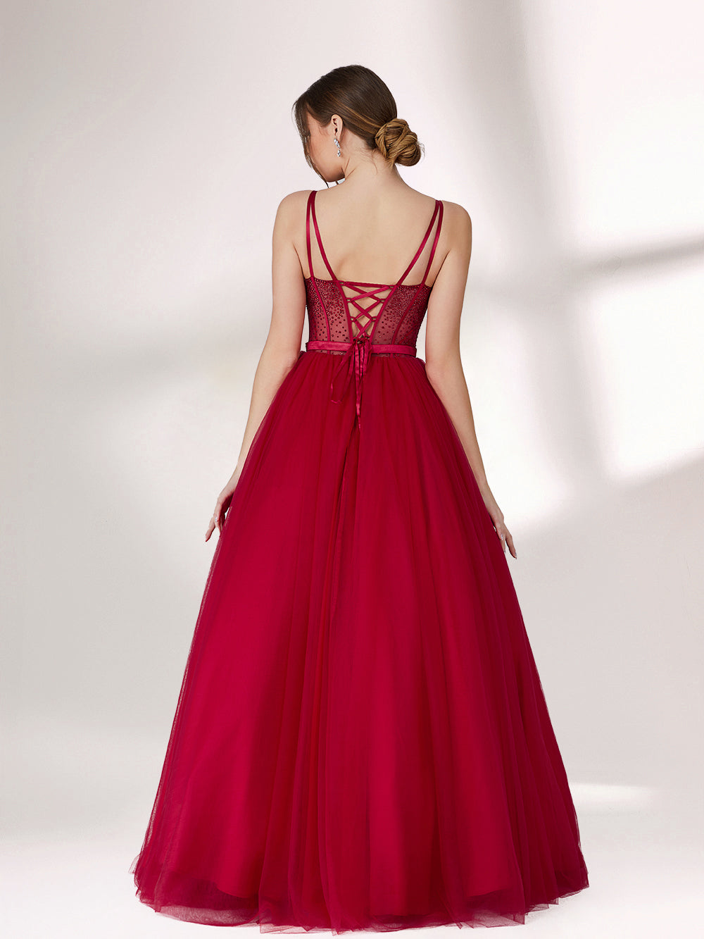 A woman stands against a light background, wearing a deep red evening gown. It features thin spaghetti straps, a sweetheart neckline with a sequined bodice that has sheer, dotted detailing. The skirt is a voluminous, flowing tulle, creating an elegant and romantic look, perfect for formal events.2