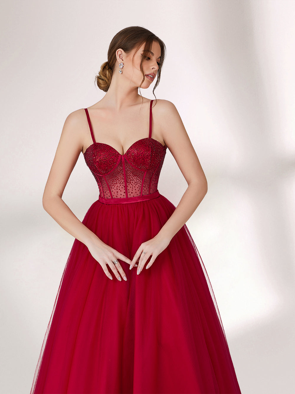 A woman stands against a light background, wearing a deep red evening gown. It features thin spaghetti straps, a sweetheart neckline with a sequined bodice that has sheer, dotted detailing. The skirt is a voluminous, flowing tulle, creating an elegant and romantic look, perfect for formal events.3
