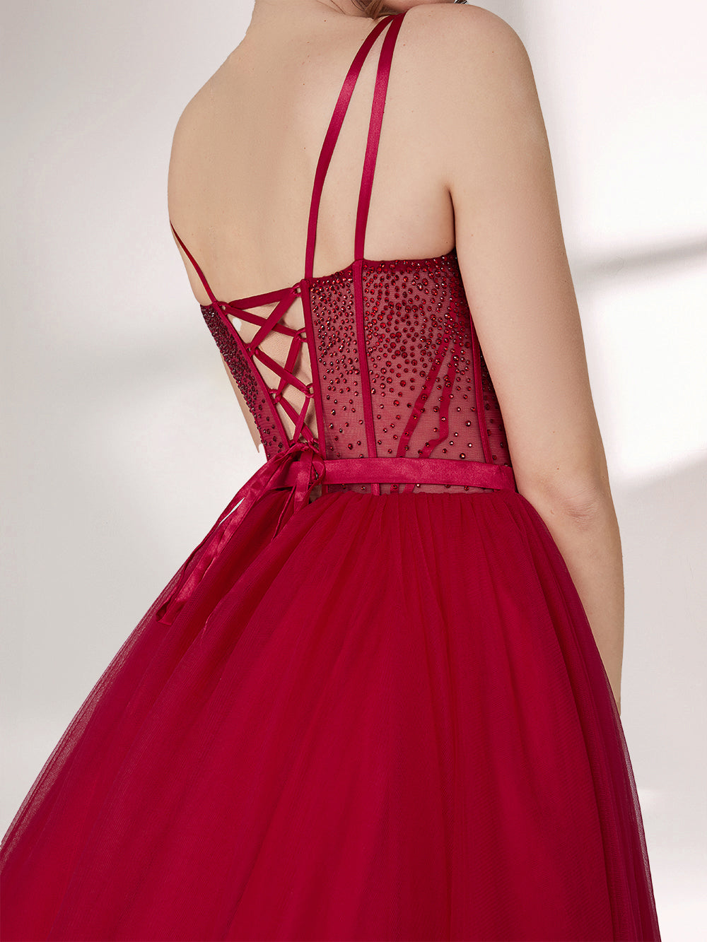 A woman stands against a light background, wearing a deep red evening gown. It features thin spaghetti straps, a sweetheart neckline with a sequined bodice that has sheer, dotted detailing. The skirt is a voluminous, flowing tulle, creating an elegant and romantic look, perfect for formal events.4