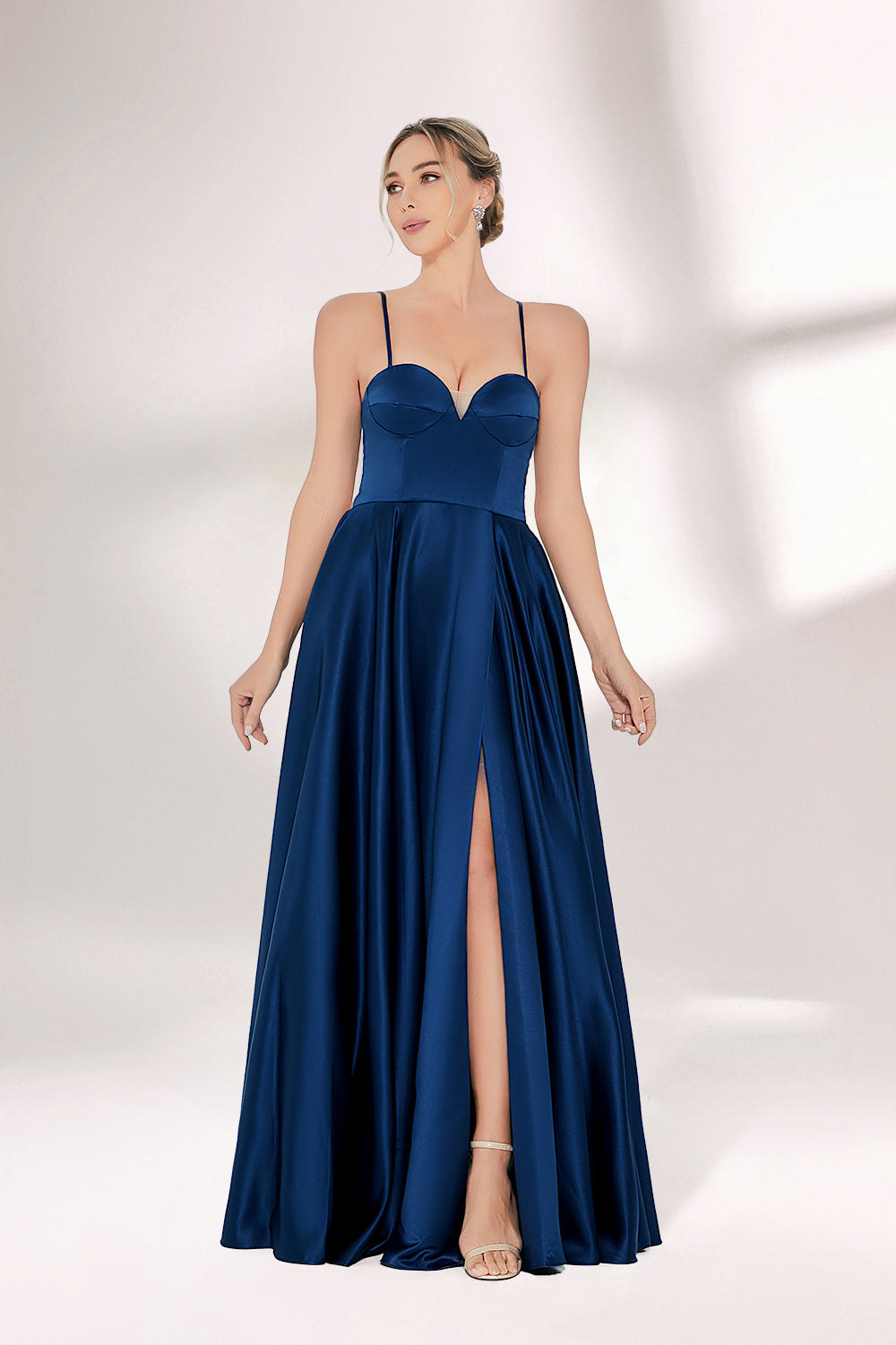 A woman with short, sleek hair and a poised demeanor wears a navy - blue satin gown. It has thin spaghetti straps, a sweetheart neckline, and a voluminous, flowing skirt. Paired with understated heels, the outfit radiates elegance, ideal for formal events like galas or weddings.06