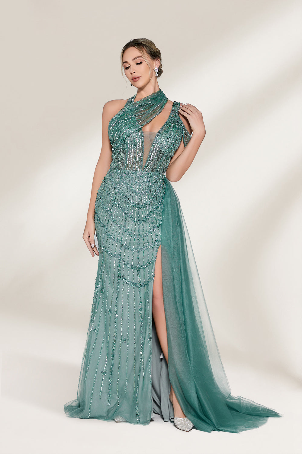 A woman with an elegant updo and a poised stance wears a teal, beaded gown. It has a high - neck, cut - out shoulder design, a form - fitting bodice, and a high side slit. A flowing tulle train adds drama. Paired with silver heels, it's perfect for formal events like galas, radiating glamour.3
