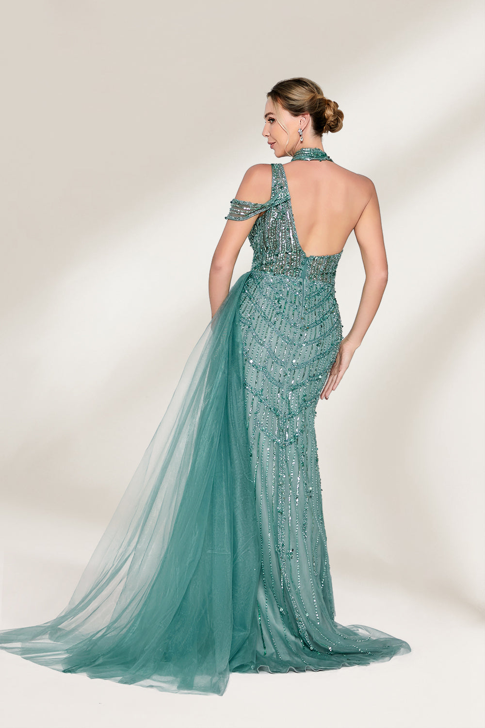 A woman with an elegant updo and a poised stance wears a teal, beaded gown. It has a high - neck, cut - out shoulder design, a form - fitting bodice, and a high side slit. A flowing tulle train adds drama. Paired with silver heels, it's perfect for formal events like galas, radiating glamour.2