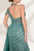 A woman with an elegant updo and a poised stance wears a teal, beaded gown. It has a high - neck, cut - out shoulder design, a form - fitting bodice, and a high side slit. A flowing tulle train adds drama. Paired with silver heels, it's perfect for formal events like galas, radiating glamour.4