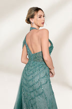 A woman with an elegant updo and a poised stance wears a teal, beaded gown. It has a high - neck, cut - out shoulder design, a form - fitting bodice, and a high side slit. A flowing tulle train adds drama. Paired with silver heels, it's perfect for formal events like galas, radiating glamour.6