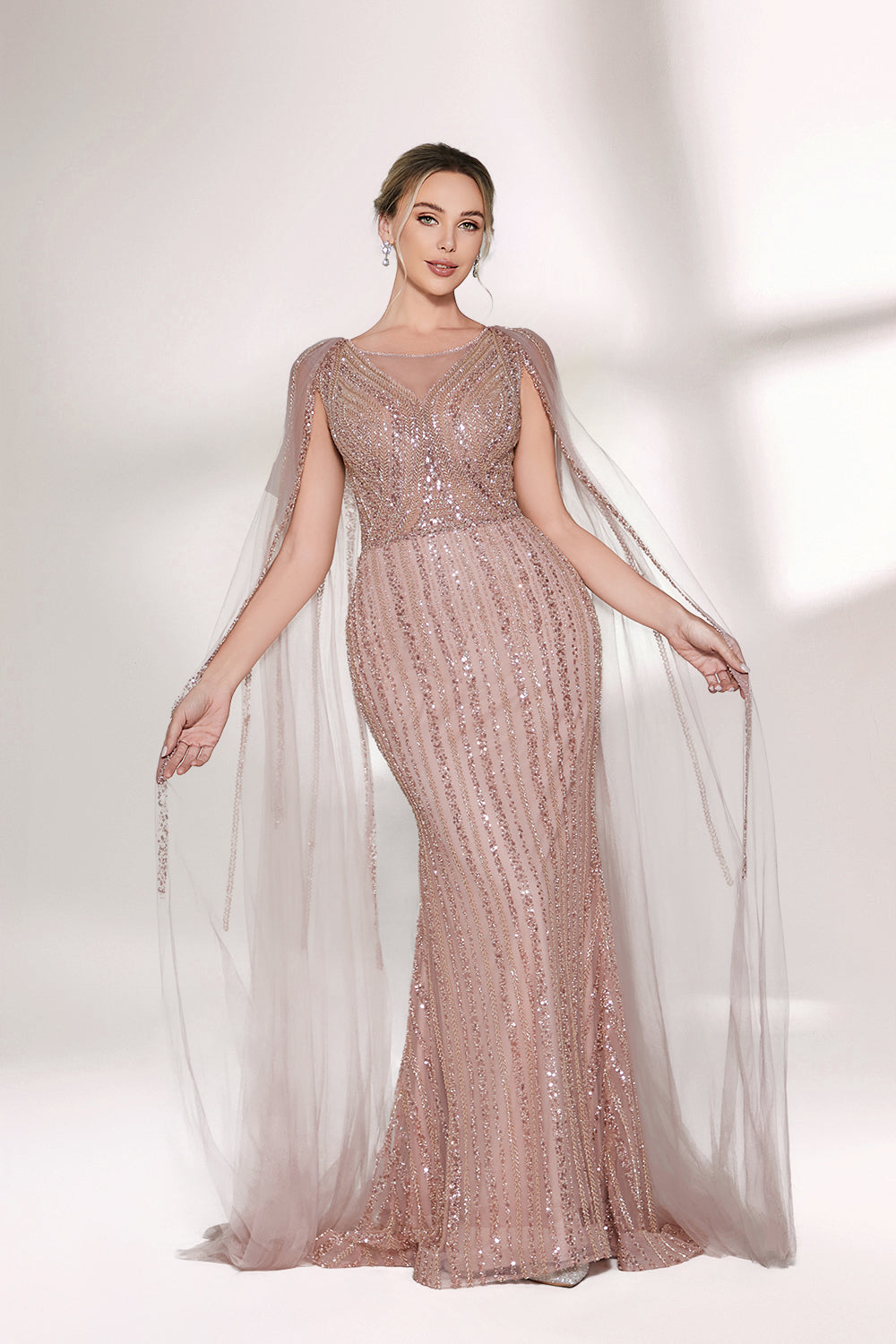 Bathed in gentle light, a woman radiates glamour in a nude - pink sequined mermaid gown. The sheer cape - like sleeves add an ethereal touch, while the body - hugging silhouette and shimmering sequins create a show - stopping, elegant look for formal events.5