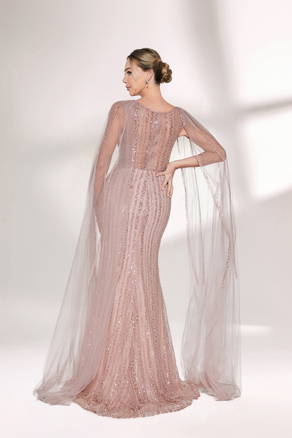 Bathed in gentle light, a woman radiates glamour in a nude - pink sequined mermaid gown. The sheer cape - like sleeves add an ethereal touch, while the body - hugging silhouette and shimmering sequins create a show - stopping, elegant look for formal events.3