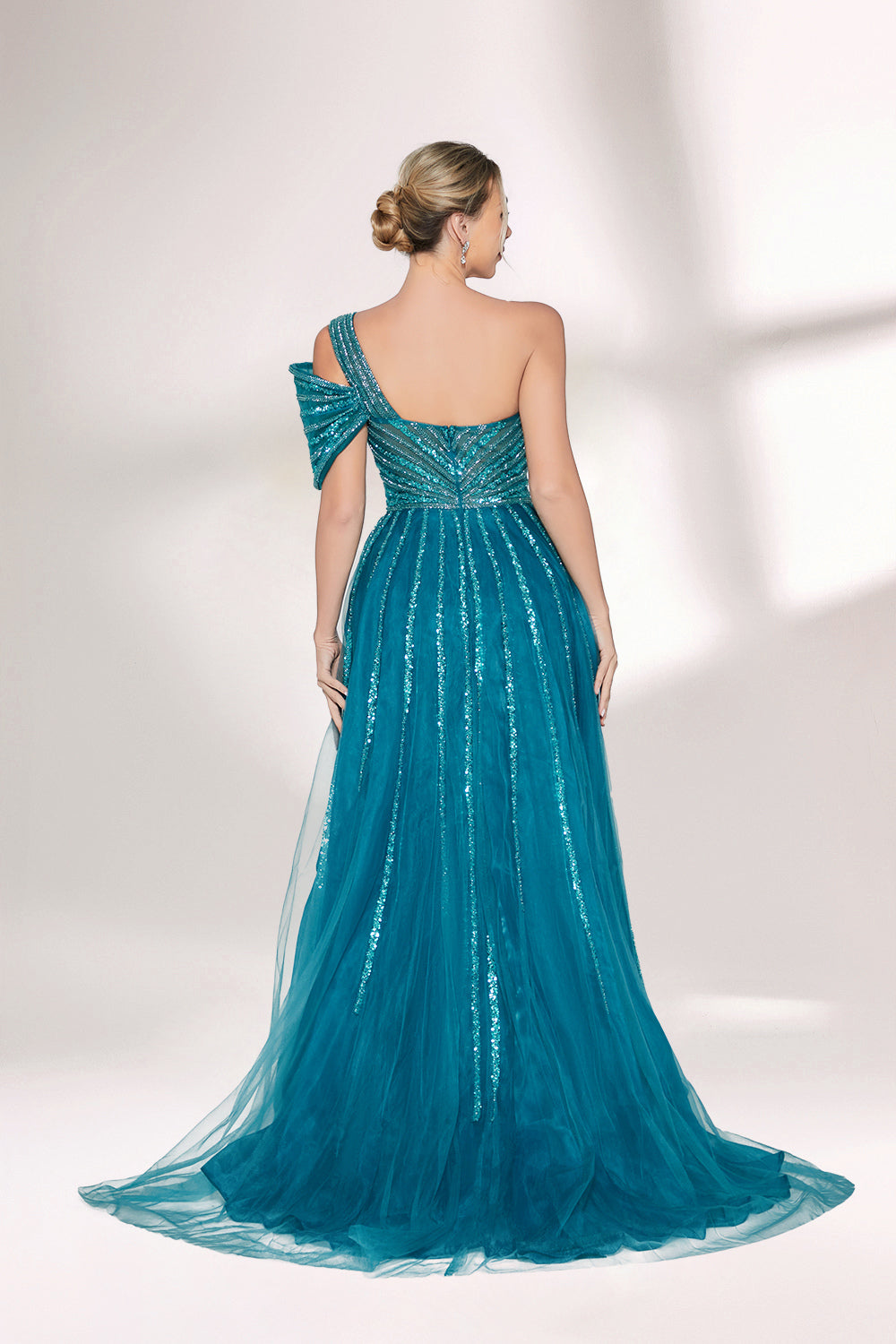 Against a light - hued backdrop, a woman dons a teal sequin gown with an one - shoulder design. It features a bow - detailed strap, a sheer waist panel, and a high side slit. The sparkling sequins and unique silhouette radiate glamour, perfect for formal dinners or galas.2
