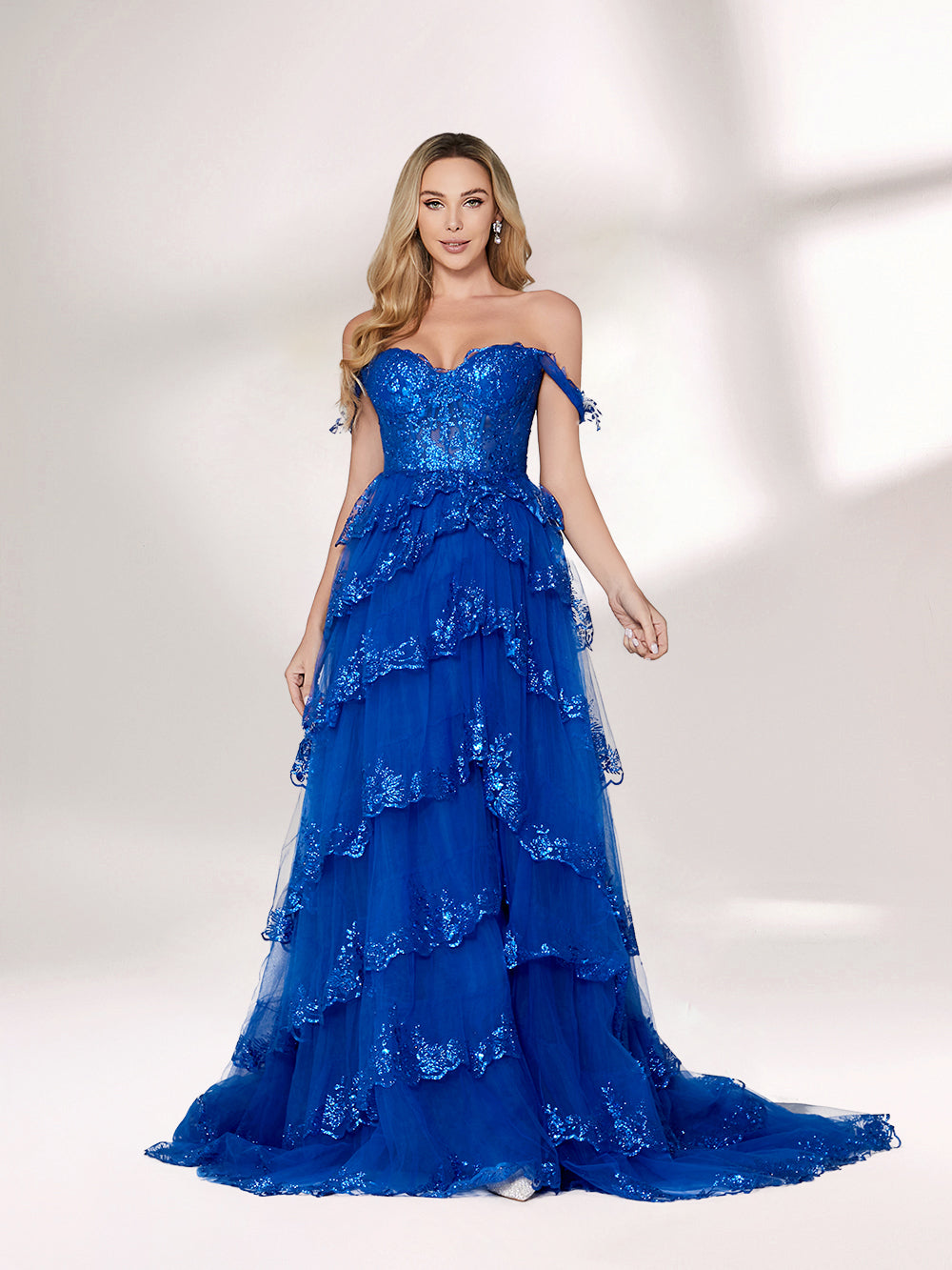 A woman stands against a light background, wearing a royal - blue tulle gown with sequin embellishments. It has an off - shoulder design, a sweetheart neckline, and a tiered skirt. The sparkling sequins and flowing fabric exude romance, perfect for formal events like weddings or galas.3
