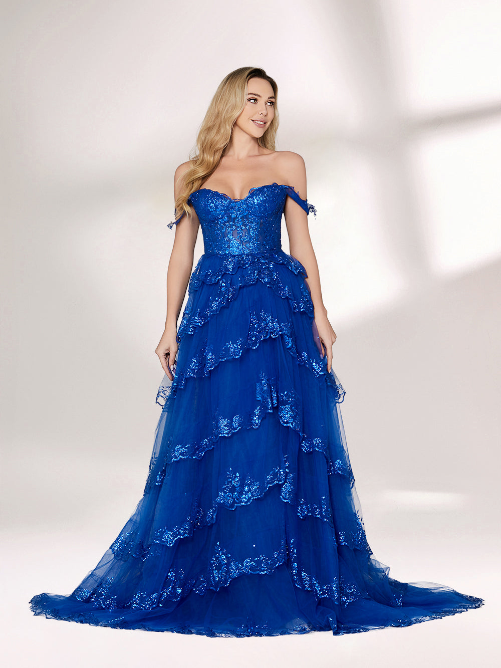 A woman stands against a light background, wearing a royal - blue tulle gown with sequin embellishments. It has an off - shoulder design, a sweetheart neckline, and a tiered skirt. The sparkling sequins and flowing fabric exude romance, perfect for formal events like weddings or galas.4