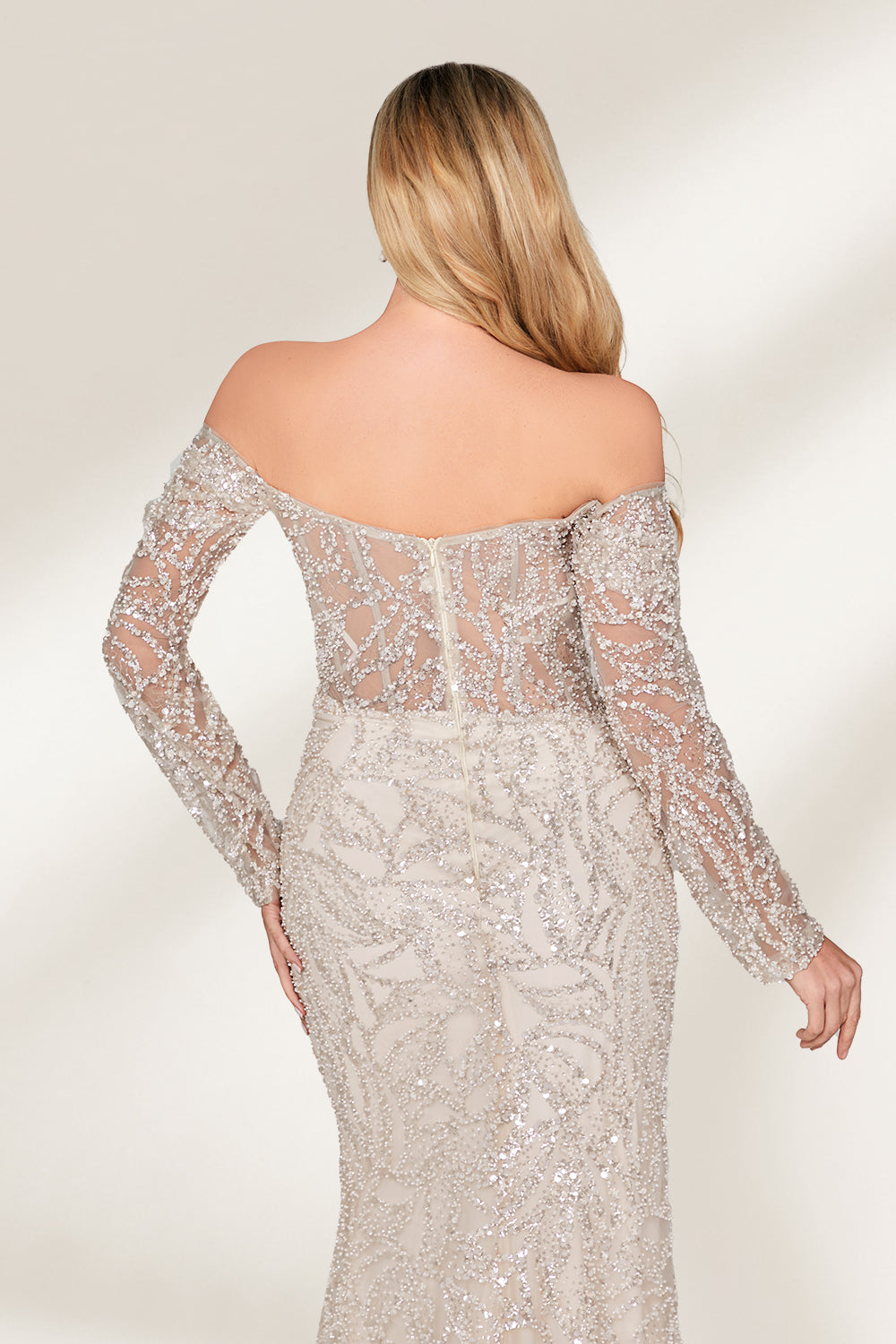 A woman with long, wavy blonde hair and a confident pose wears a silver - toned, fully beaded gown. It has an off - the - shoulder design, sheer long sleeves, and a high side slit. Paired with matching heels, the outfit radiates glamour, perfect for formal events like galas or award ceremonies.5