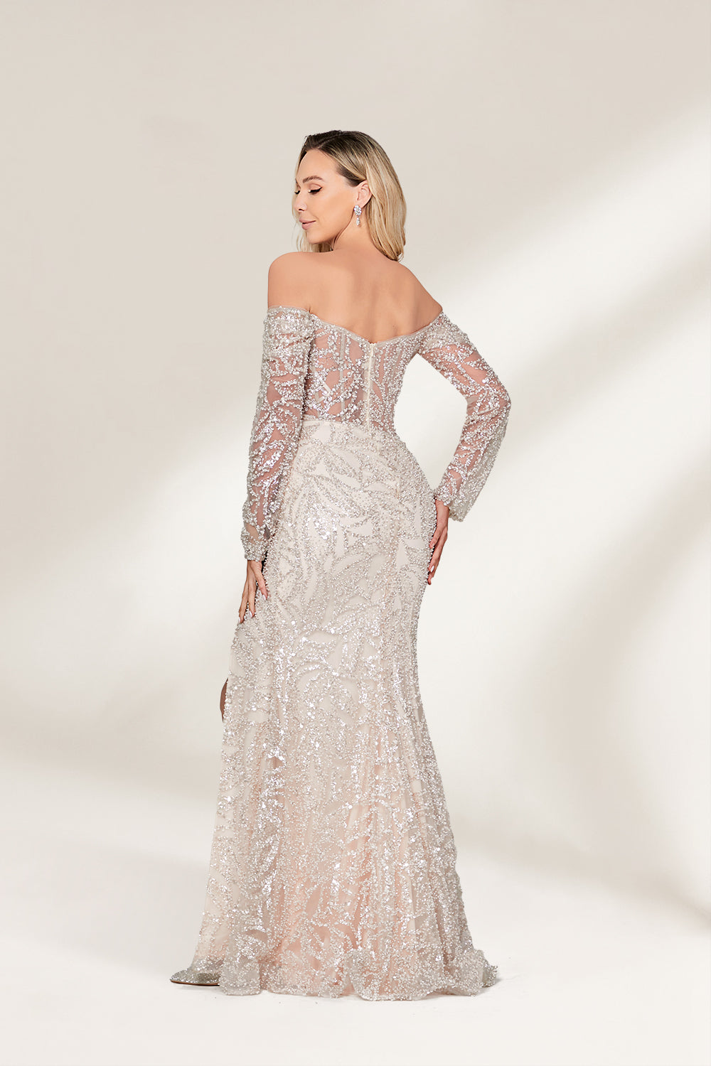 A woman with long, wavy blonde hair and a confident pose wears a silver - toned, fully beaded gown. It has an off - the - shoulder design, sheer long sleeves, and a high side slit. Paired with matching heels, the outfit radiates glamour, perfect for formal events like galas or award ceremonies.2