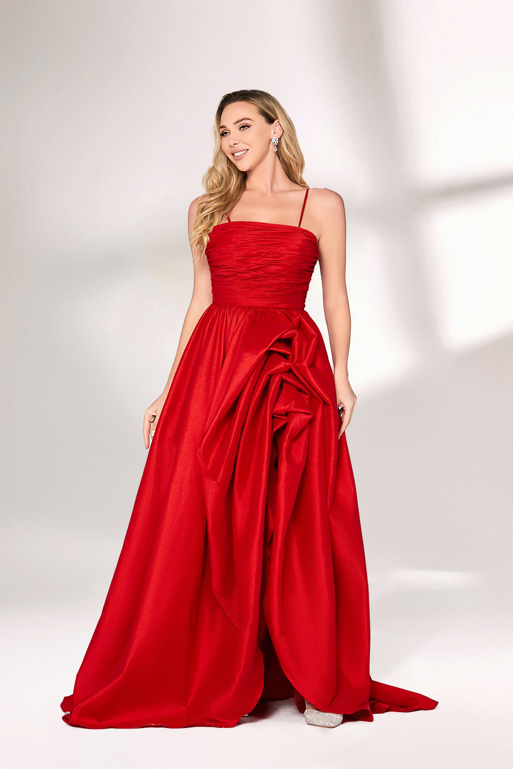 A woman with long, wavy blonde hair and a bright smile wears a vibrant red satin gown. It has thin spaghetti straps, a ruched bodice, and a voluminous, flowing skirt with a subtle train. Paired with simple, light - colored heels, the outfit exudes elegance, perfect for formal events like galas or weddings.01