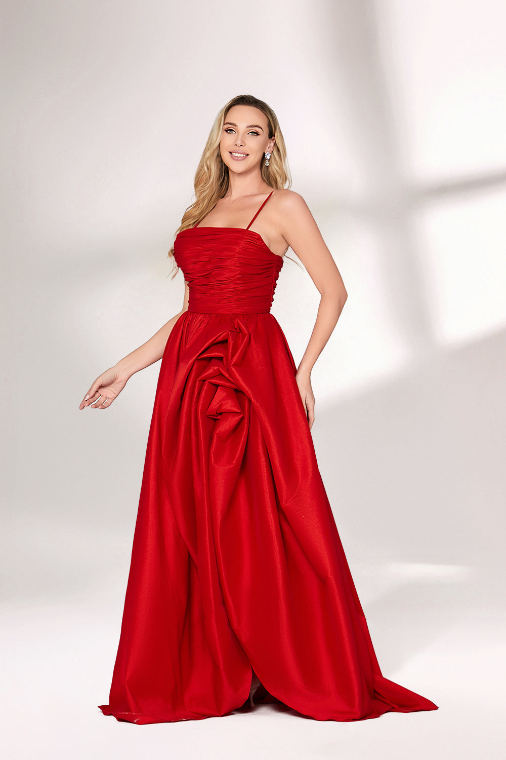 A woman with long, wavy blonde hair and a bright smile wears a vibrant red satin gown. It has thin spaghetti straps, a ruched bodice, and a voluminous, flowing skirt with a subtle train. Paired with simple, light - colored heels, the outfit exudes elegance, perfect for formal events like galas or weddings.05