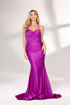 A woman with long, wavy blonde hair and a confident pose wears a vivid purple satin mermaid gown. It has thin straps, a sweetheart neckline, and a figure-hugging fit that shows her curves. The skirt flows to the floor with a slight train. Paired with simple heels, the outfit suits formal events, radiating elegance and charm.002