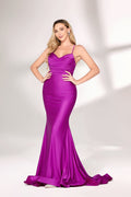 A woman with long, wavy blonde hair and a confident pose wears a vivid purple satin mermaid gown. It has thin straps, a sweetheart neckline, and a figure-hugging fit that shows her curves. The skirt flows to the floor with a slight train. Paired with simple heels, the outfit suits formal events, radiating elegance and charm.01