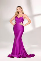 A woman with long, wavy blonde hair and a confident pose wears a vivid purple satin mermaid gown. It has thin straps, a sweetheart neckline, and a figure-hugging fit that shows her curves. The skirt flows to the floor with a slight train. Paired with simple heels, the outfit suits formal events, radiating elegance and charm.01