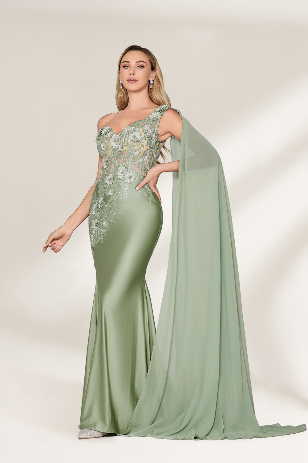 A woman stands against a light background, wearing a sage - green satin gown. It features a one - shoulder design with a flowing cape, floral lace embroidery on the bodice and skirt, and a mermaid silhouette. The elegant details and unique cape create a sophisticated look, perfect for formal events like galas or weddings.3