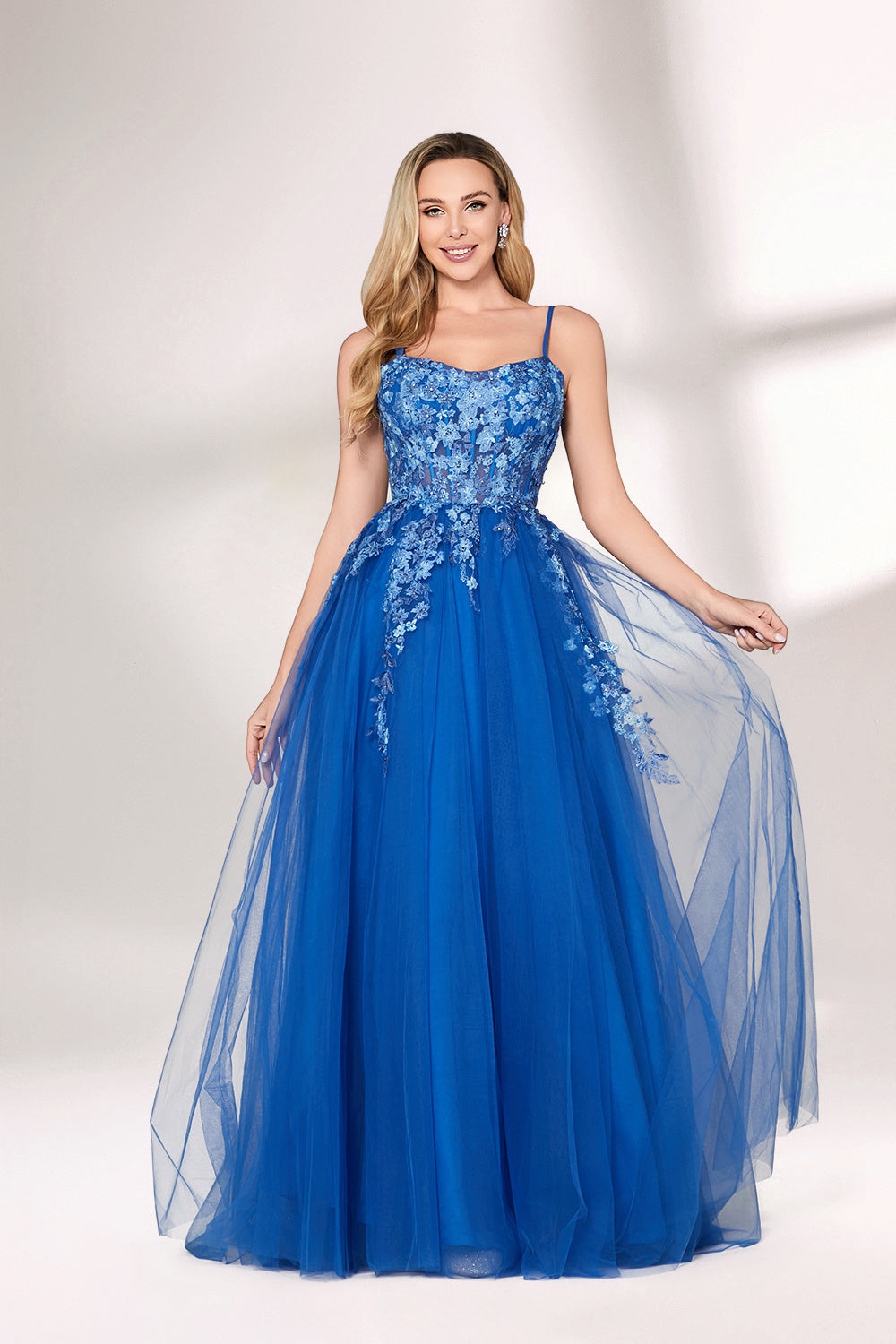 A woman stands against a light background, wearing a bright blue evening gown. It features thin spaghetti straps, a sweetheart neckline, and a bodice adorned with delicate floral lace embroidery. The voluminous tulle skirt flows elegantly, creating a romantic and glamorous look, perfect for formal events.1