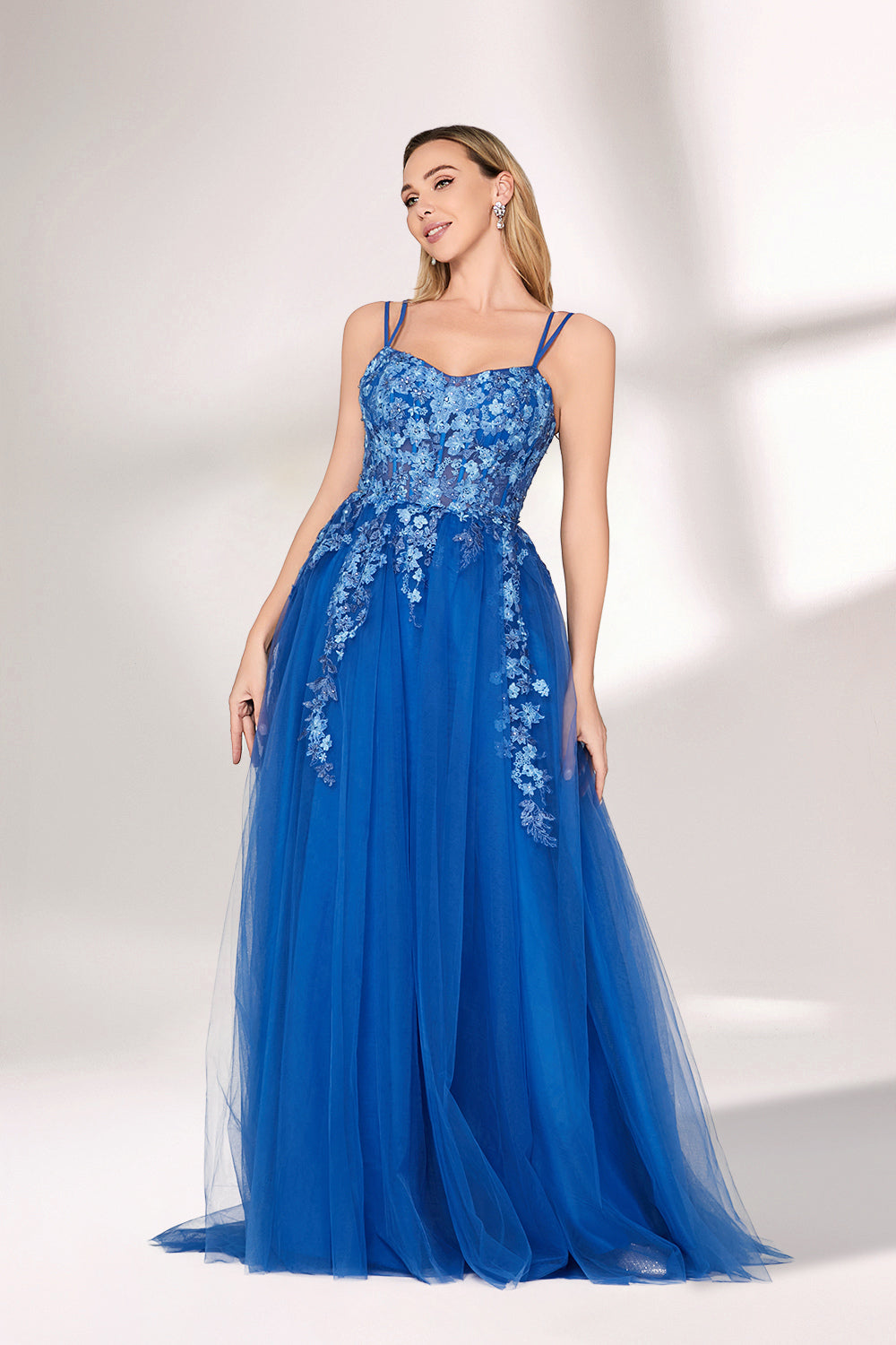 A woman stands against a light background, wearing a bright blue evening gown. It features thin spaghetti straps, a sweetheart neckline, and a bodice adorned with delicate floral lace embroidery. The voluminous tulle skirt flows elegantly, creating a romantic and glamorous look, perfect for formal events.4