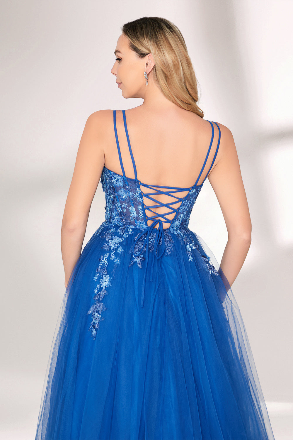 A woman stands against a light background, wearing a bright blue evening gown. It features thin spaghetti straps, a sweetheart neckline, and a bodice adorned with delicate floral lace embroidery. The voluminous tulle skirt flows elegantly, creating a romantic and glamorous look, perfect for formal events.6