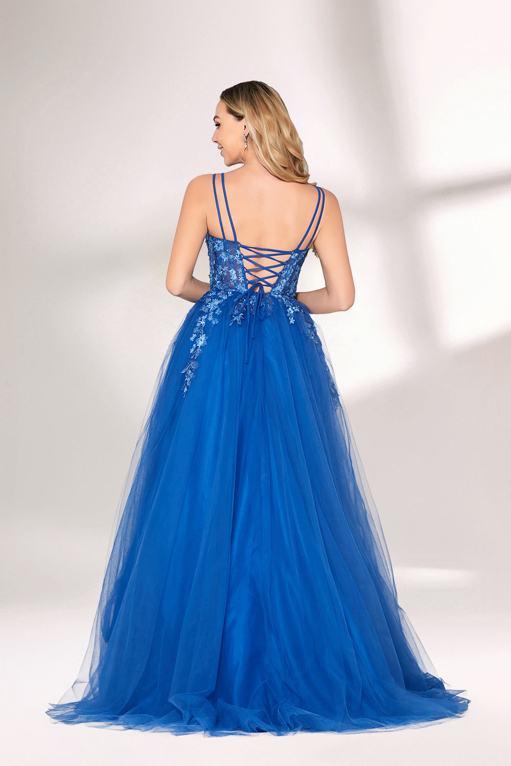 A woman stands against a light background, wearing a bright blue evening gown. It features thin spaghetti straps, a sweetheart neckline, and a bodice adorned with delicate floral lace embroidery. The voluminous tulle skirt flows elegantly, creating a romantic and glamorous look, perfect for formal events.2