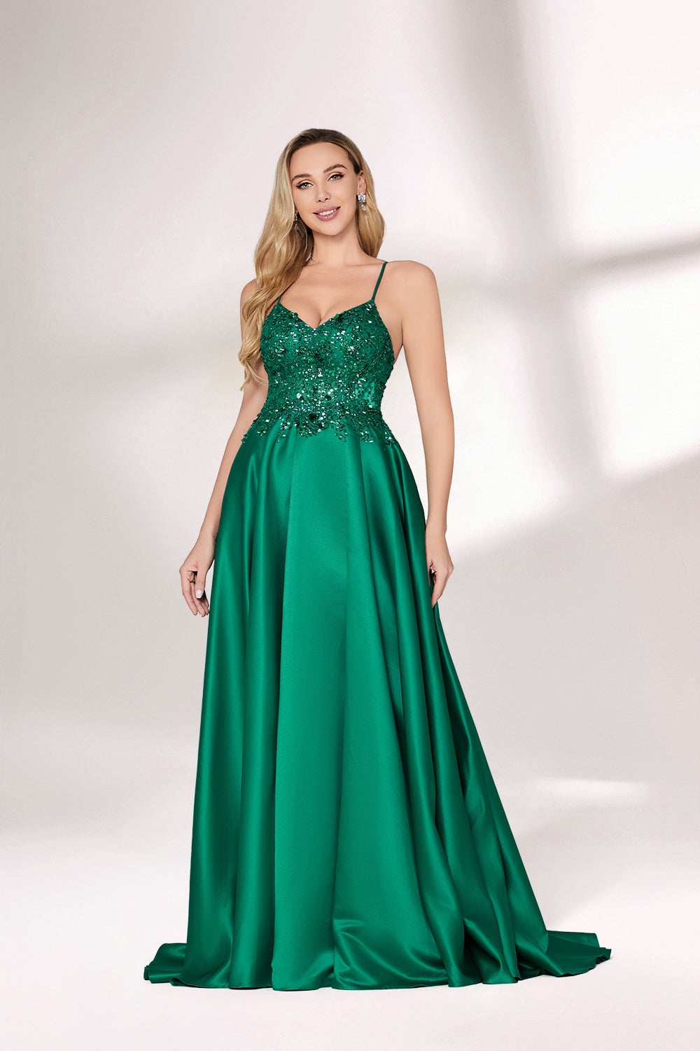 A woman with long, wavy blonde hair and a confident pose wears a rich green satin gown. It features thin spaghetti straps, a beaded and sequined bodice, and a high side slit. Paired with silver heels, the outfit radiates elegance, ideal for formal events like galas or evening receptions.06