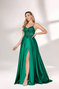 A woman with long, wavy blonde hair and a confident pose wears a rich green satin gown. It features thin spaghetti straps, a beaded and sequined bodice, and a high side slit. Paired with silver heels, the outfit radiates elegance, ideal for formal events like galas or evening receptions.01