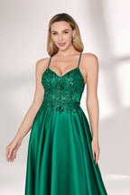 A woman with long, wavy blonde hair and a confident pose wears a rich green satin gown. It features thin spaghetti straps, a beaded and sequined bodice, and a high side slit. Paired with silver heels, the outfit radiates elegance, ideal for formal events like galas or evening receptions.05