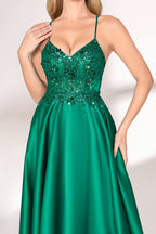 A woman with long, wavy blonde hair and a confident pose wears a rich green satin gown. It features thin spaghetti straps, a beaded and sequined bodice, and a high side slit. Paired with silver heels, the outfit radiates elegance, ideal for formal events like galas or evening receptions.04