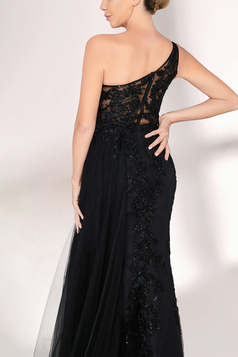 A woman dons a stunning black one - shoulder evening gown. The bodice is intricately adorned with beadwork and embroidery, adding a touch of luxury. The dress has a form - fitting silhouette that hugs the curves, and a high side slit reveals a hint of leg. A sheer, flowing overlay cascades down from the side, enhancing the gown's elegance. Paired with simple strappy silver heels, she stands gracefully against a light - colored backdrop, making the dress perfect for formal galas or upscale events.04